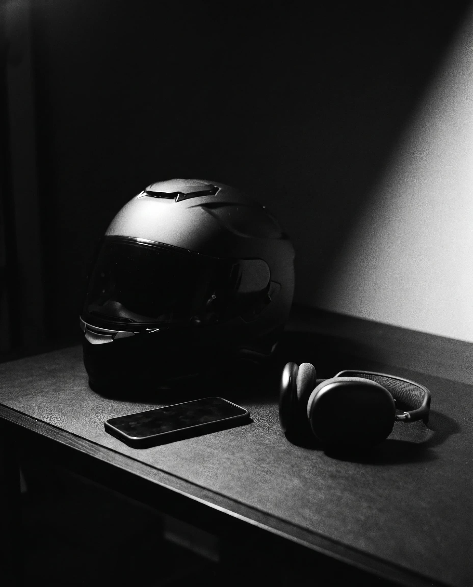A motorcycle helmet beside a corded desk telephone in hard black-and-white light